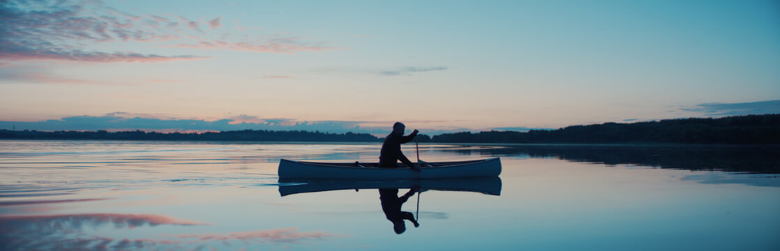 Man canoeing in a traditional wooden boat on a large lake at dawn