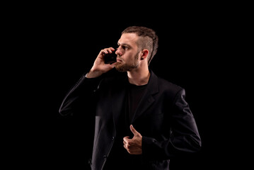 Portrait of a business man in a black suit and with a telephone isolated on black background.