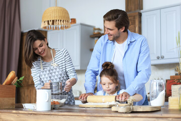 Cute little girl and her parents are having fun while cooking in kitchen at home together.