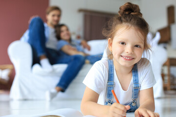Smiling happy family sit relax on couch in living room watch little daughter drawing in album with colorful pencils. Happy weekends at home.