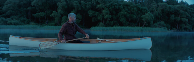 Portrait of mid 50s man canoeing alone boat on a large lake at dawn
