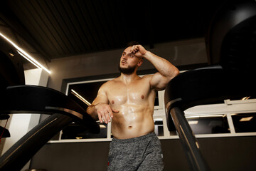 Young strong sporty man sitting on gym bench suffering and serious in a gym