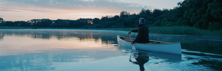Fototapeta na wymiar Man canoeing in a traditional wooden boat on a large lake at dawn