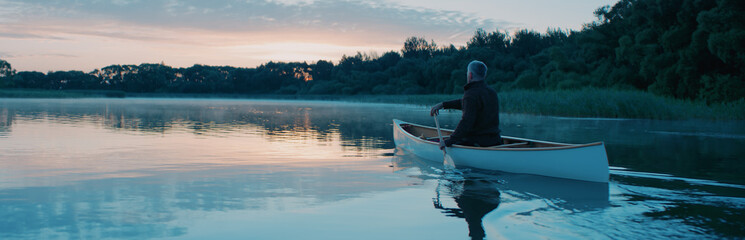 Man canoeing in a traditional wooden boat on a large lake at dawn