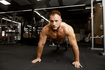 Fototapeta na wymiar Sport motivation for people. Front view of young handsome man in sportswear doing push-up at gym