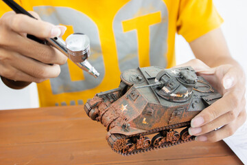 man painting scale model WW2 tank on table. Hobbie.
