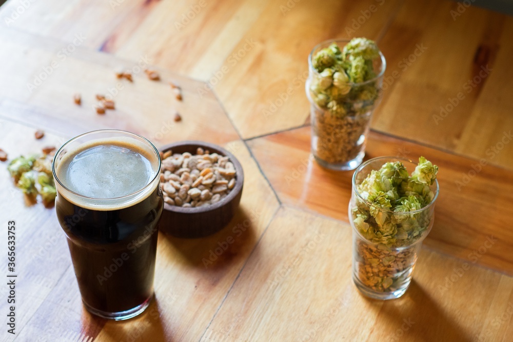 Sticker High angle shot of a glass of beer next to peanuts, pine nuts, and hops on a wooden surface