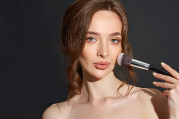 Portrait of the beautiful brunette woman with make-up brushes near face. Girl posing over Gray background. Clean natural makeup.
