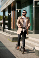 Elegant businessman in sunglasses, coat and pants moving on electric scooter