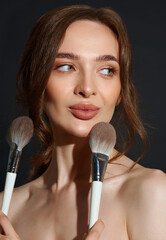 Portrait of the beautiful brunette woman with make-up brushes near face. Girl posing over Gray background. Clean natural makeup.