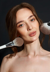 Portrait of the beautiful brunette woman with make-up brushes near face. Girl posing over Gray background. Clean natural makeup.