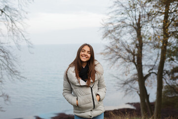 Cute young smiling pleased woman with a lovely sense of humour and perfect white smile standing against beatiful sea view with trees 