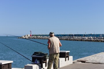 Obraz premium Pesaro, Italy - 9 july 2020: an old fisherman in fishing on the pier of the harbor