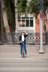 Young woman with electric scooter waiting for the green light to cross the road