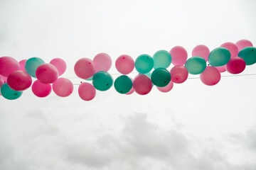 Garland of multicolored balloons pink and green on a light background of cloudy sky