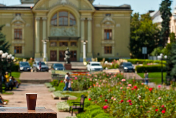 Brown paper cup on a background of urban architecture. Coffee on a marble border. The houses of the old town are blurred in the background. Sharpness on coffee. Layout for design.