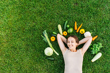 Healthy food and healthy mind. Happy young woman lays surrounded fresh vegetables on green grass...