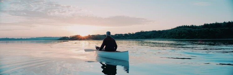 Man canoeing in a traditional wooden boat on a large lake at dawn, enjoying sunrise. Shot on RED cinema camera with 2x anamorphic lens