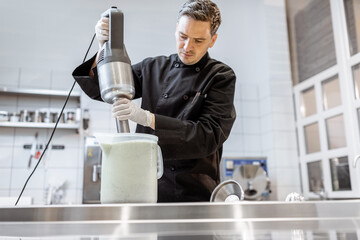 Chef cook mixing ingredients with professional blender, making a base for ice cream production at the kitchen or small manufacturing