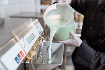 Chef pouring mixed milk base into the ice cream machine or freezer, close-up