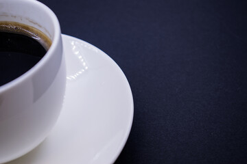 half of a white Cup with a saucer on the left on a black background