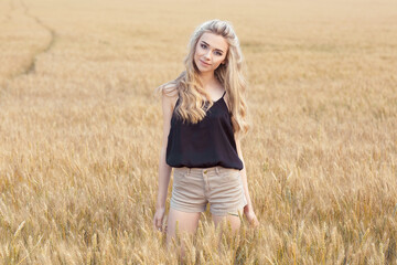 Smiling beautiful woman girl in a wheat field on the background of the setting sun.