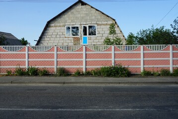long concrete pink fence on the street in front of a brick house on a gray asphalt road