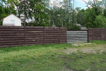 brown fence wall and gray gate made of boards outside in green grass