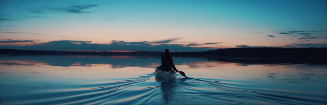 WIDE Man canoeing in a traditional wooden boat on a large lake at dawn. Shot on RED cinema camera with 2x anamorphic lens