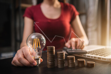 Business woman hand holding lightbulb with coins stack on desk. concept saving energy and money at office.