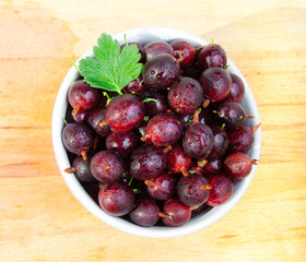 Fresh red gooseberries  in a cup on wooden background