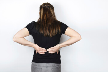 The woman is holding her back with both hands because she is experiencing severe sharp pain in her lower back. The woman sits all day at work and moves little. Rear view