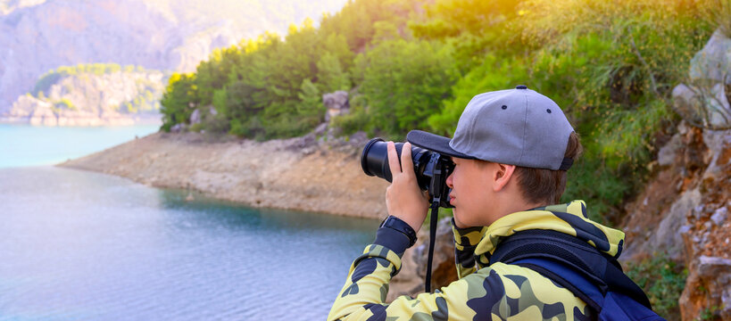 Boy photographer holding digital camera and shooting landscape of lake in the mountains