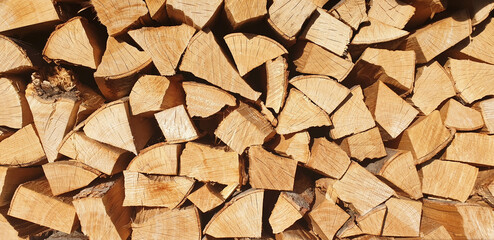 The background of stacked chopped firewood on a sunny day. Panorama.