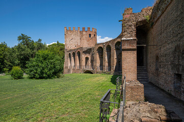 Fototapeta premium The Aurelian Walls of Rome at Porta San Sebastiano seen from inside the city. Brick support arches and cobblestone walkway. The walls border whit a vast lawn with trees. Clear day with clouds. Italy