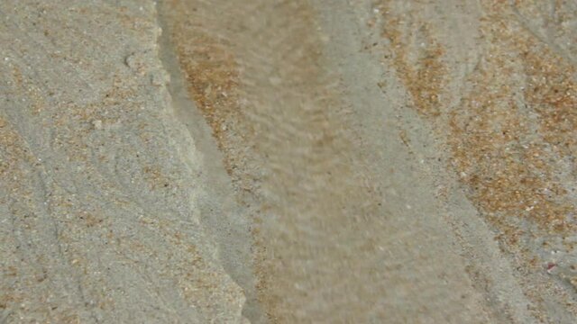 Water and sand flows into the sea like a little river on beach
