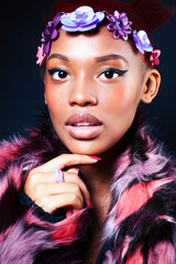 young pretty african american woman in spotted fur coat and flowers jewelry posing on black background