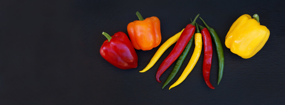Peppers and chillis on black slate, header