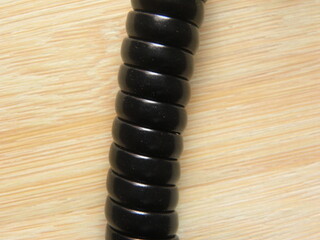 Close up of black spiral landline telephone handset connector cable jack kept on wooden table
