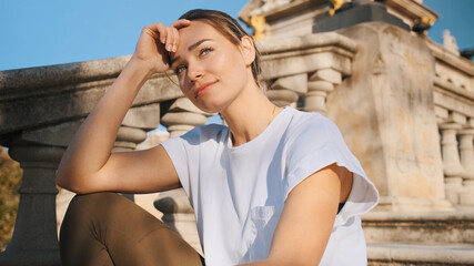 Beautiful girl in t-shirt sitting on old stairs on street and dreaming. Thinking expression