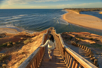 Woman walking down iconic Port Noarlunga boardwalk while watching spectacular sunset view, South...