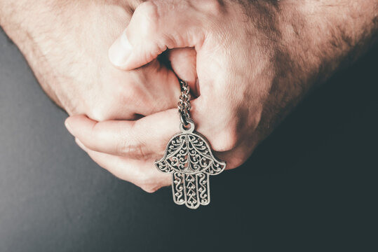 close-up of folded hands holding Hamsa amulet also known as Hand of Fatima used to protect against evil eye,, unluckiness, illness and bad fortune