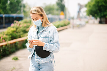 Young woman wearing antibacterial mask using phone in a city.