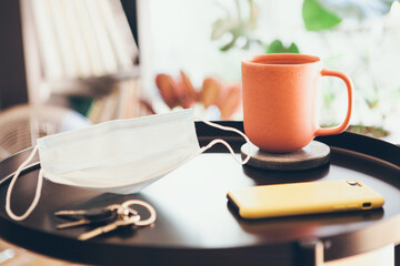 Staying home after work day, relaxing, offline, taking off the surgical mask. Feeling safe. Close-up of round black table with cup of tea and face mask. New normal. Selective focus, lifestyle photo.