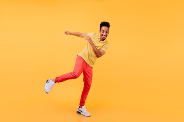 Fototapeta na wymiar Full-length portrait of joyful african male model dancing in yellow shoes. Cheerful black man enjoying photoshoot on bright background.