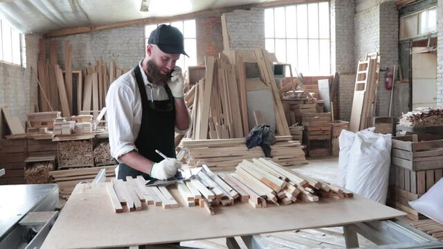Carpenter in his own woodshop using a tablet pc and writes notes while being  in his workspace. Small business concept
