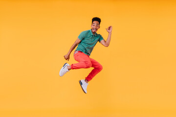 Joyful short-haired guy jumping on yellow background. Indoor photo of stunning male model in green...
