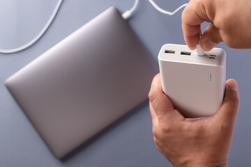 close-up of man's hands charge laptop with power bank by USB cable. Tech device charge concept. blue background. top view