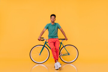 Full-length portrait of confident african man standing in front of his bike. Studio shot of...