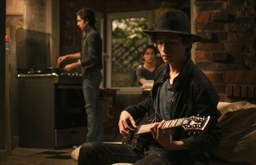 Boy playing guitar in the kitchen behind two others